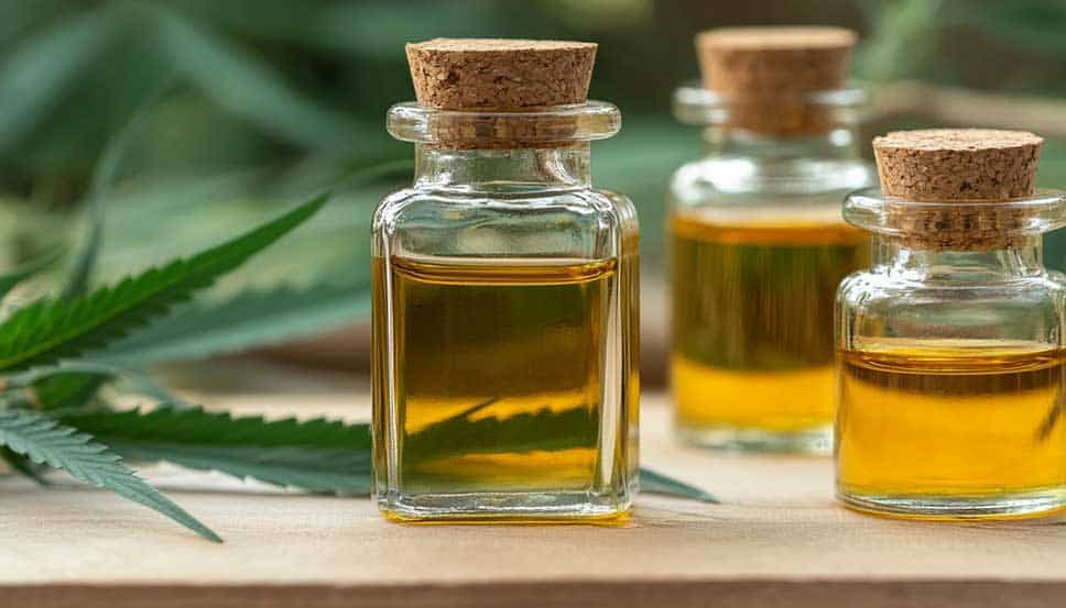Close-up of a golden cannabis oil dropper bottle on wood surface, illustrating how to make cannabis oil at home